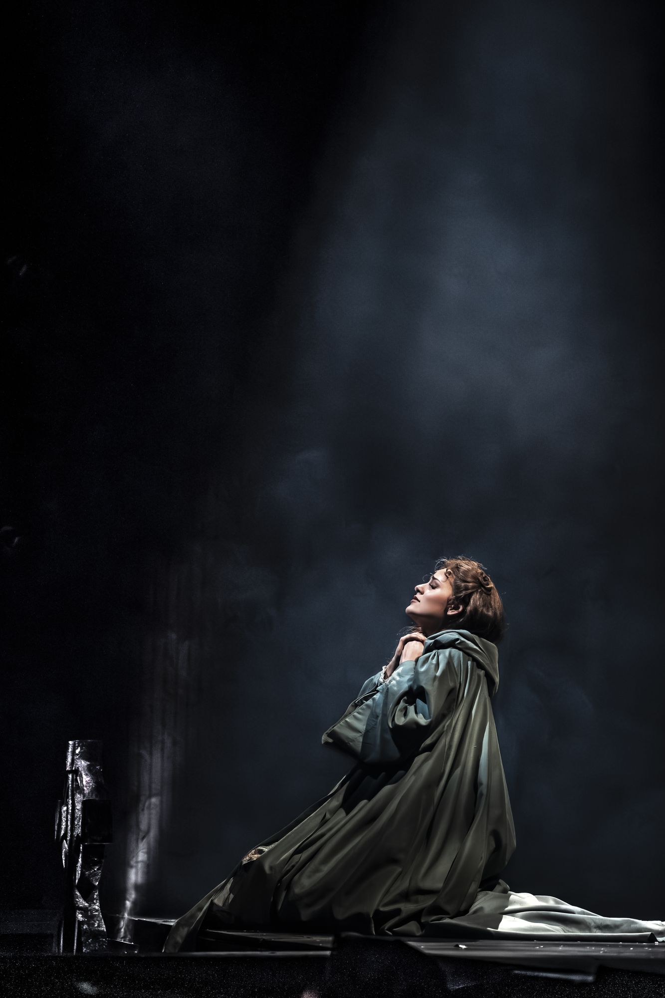 Christine Daaé kneeling in stage smoke under a narrow spotlight