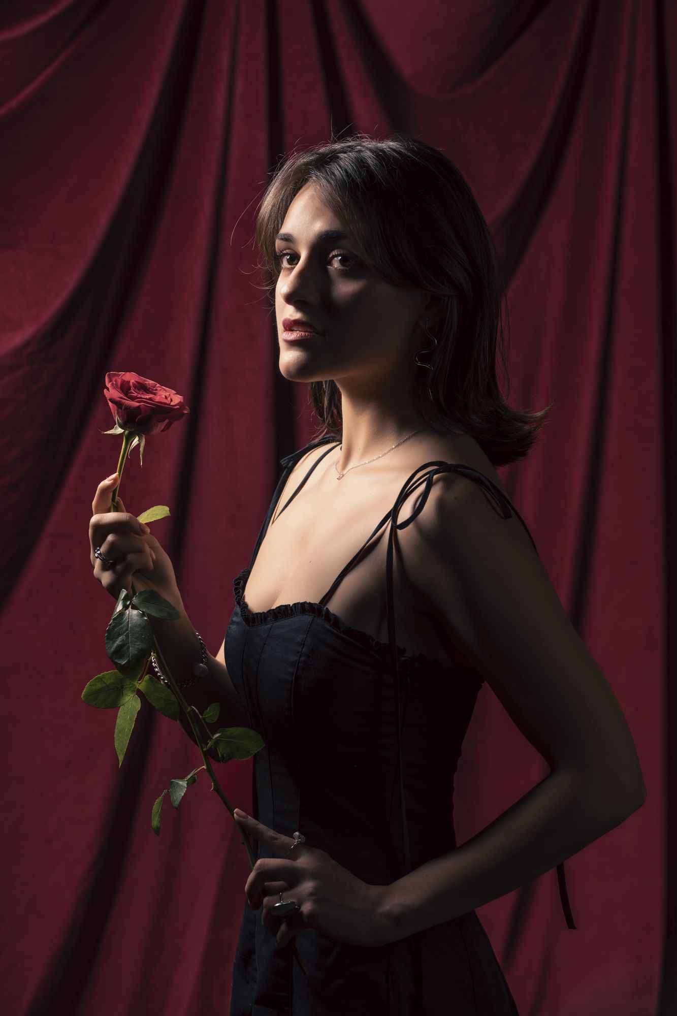 Standing with a red rose against a crimson curtain
