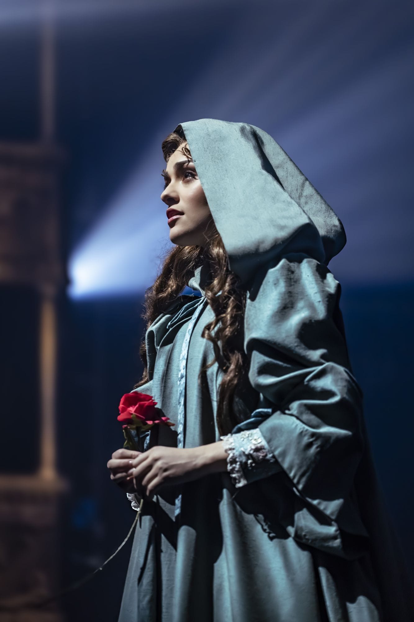 Christine Daaé in a hooded cloak holding a single red rose